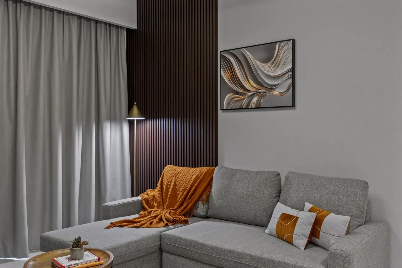Gray sectional sofa with an orange throw blanket and matching pillows in a modern living room.