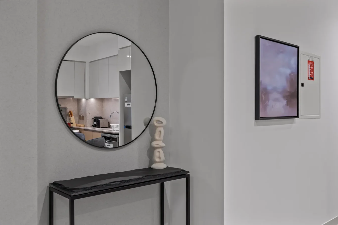 Round black-framed mirror on a gray wall reflecting a white, modern kitchen with cabinets and appliances.