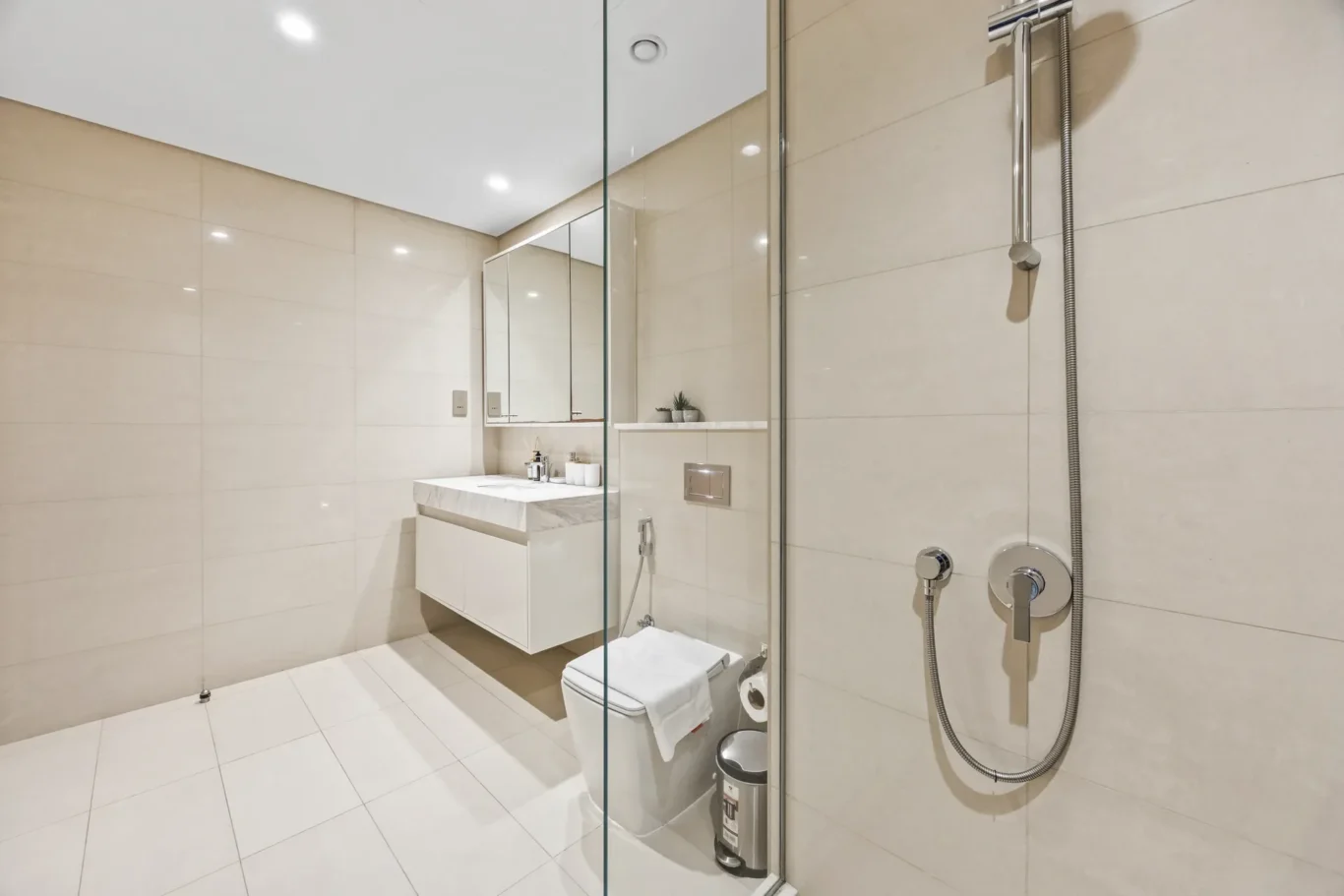 Modern bathroom with a glass shower enclosure, wall-mounted vanity, and large mirror, beige tiled walls and floor.
