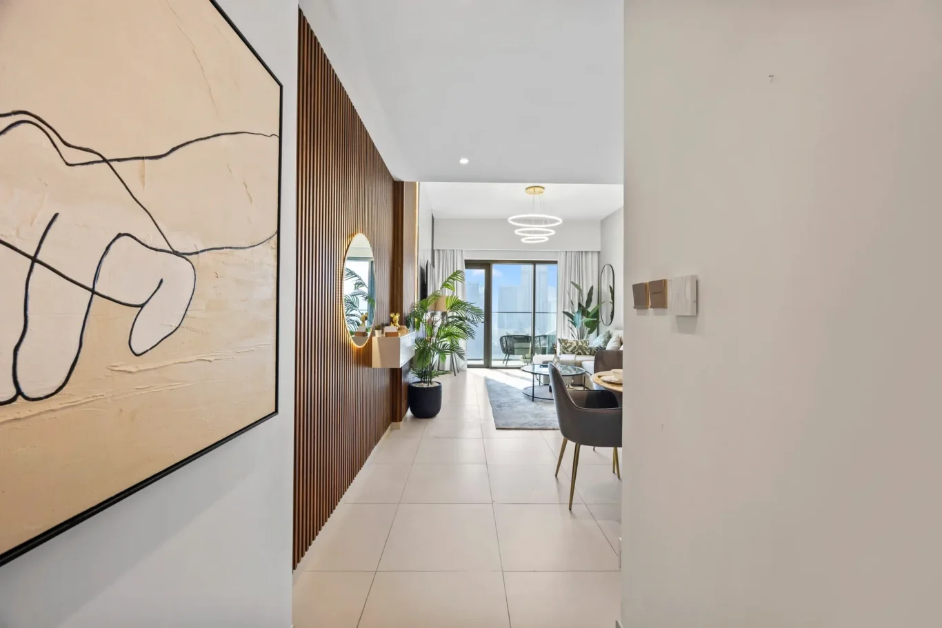 Modern corridor with a wooden slat wall, large abstract painting, and entry to a bright living area with plants and circular hanging light fixtures.