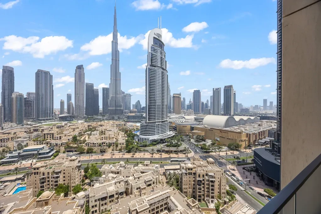 Panoramic view of Dubai skyline with the Burj Khalifa and surrounding skyscrapers against a blue sky; foreground shows beige residential buildings.
