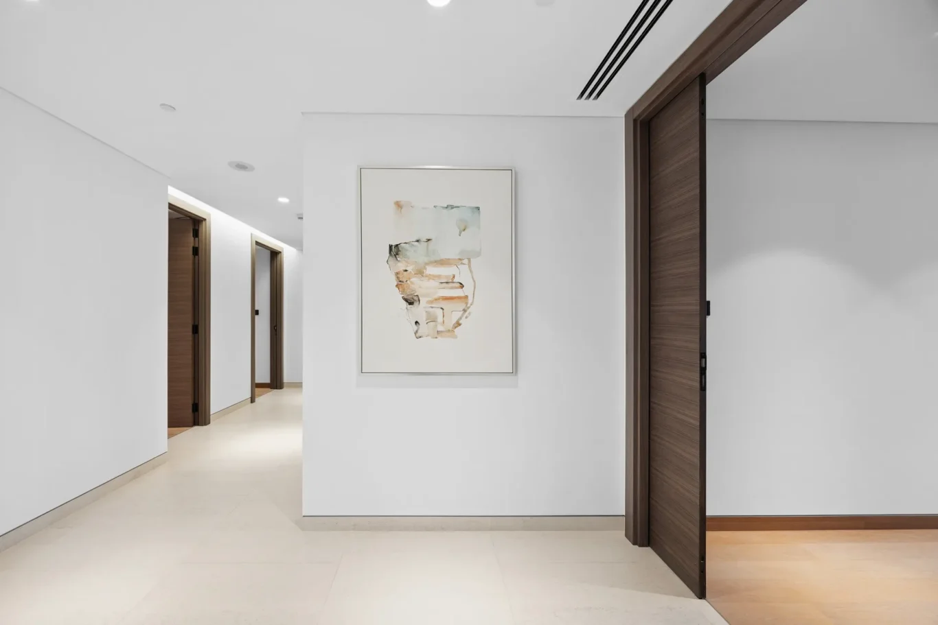 White hallway with a framed abstract painting on a central wall panel between open wooden doors on both sides, soft neutral lighting.
