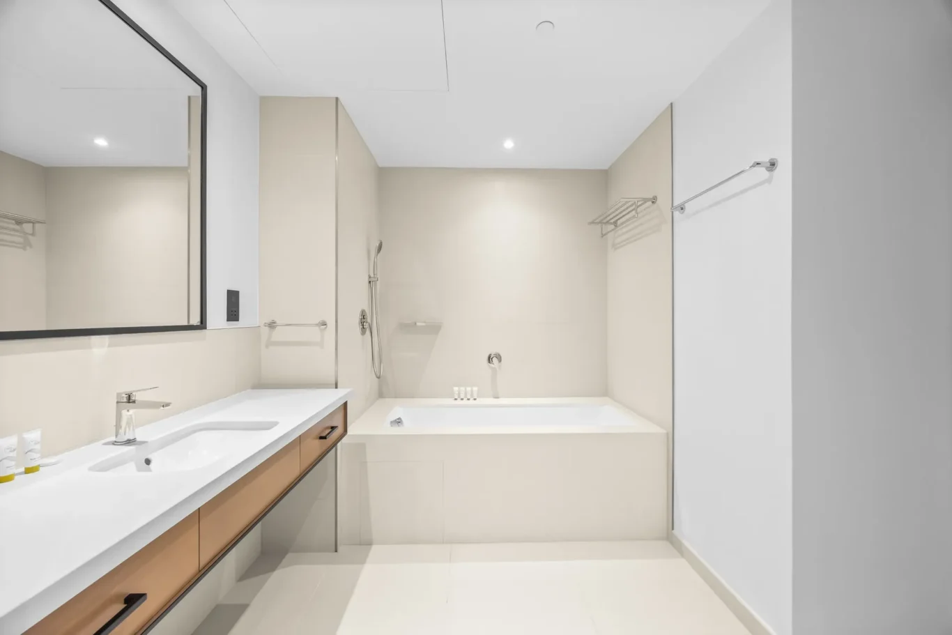 Modern bathroom with a double-sink vanity, large mirror, beige walls, and a built-in bathtub.