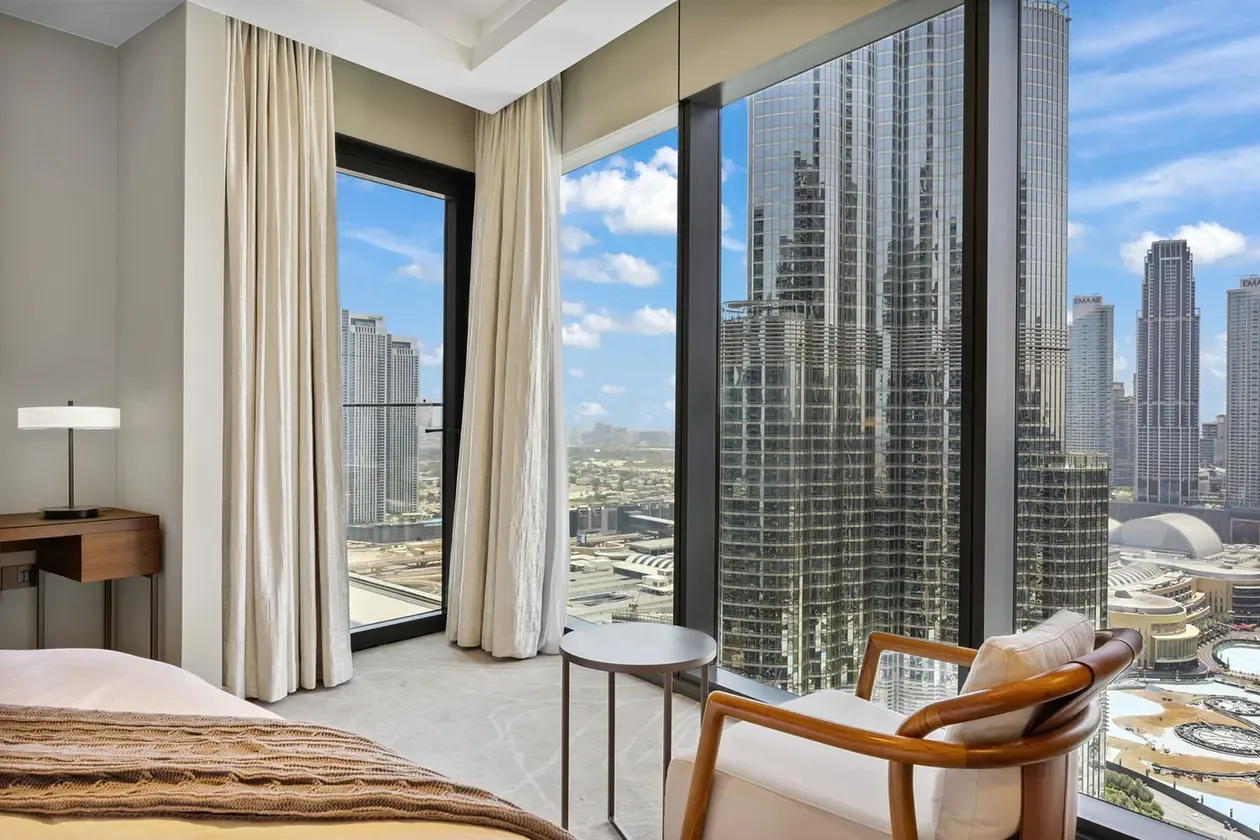 Hotel room with floor-to-ceiling windows overlooking a city skyline and modern skyscrapers.