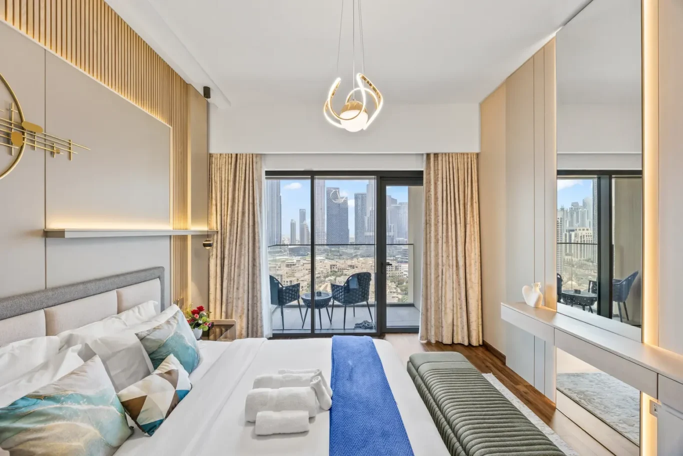 Modern hotel bedroom with a large bed, blue runner, and city skyline visible through glass balcony doors.