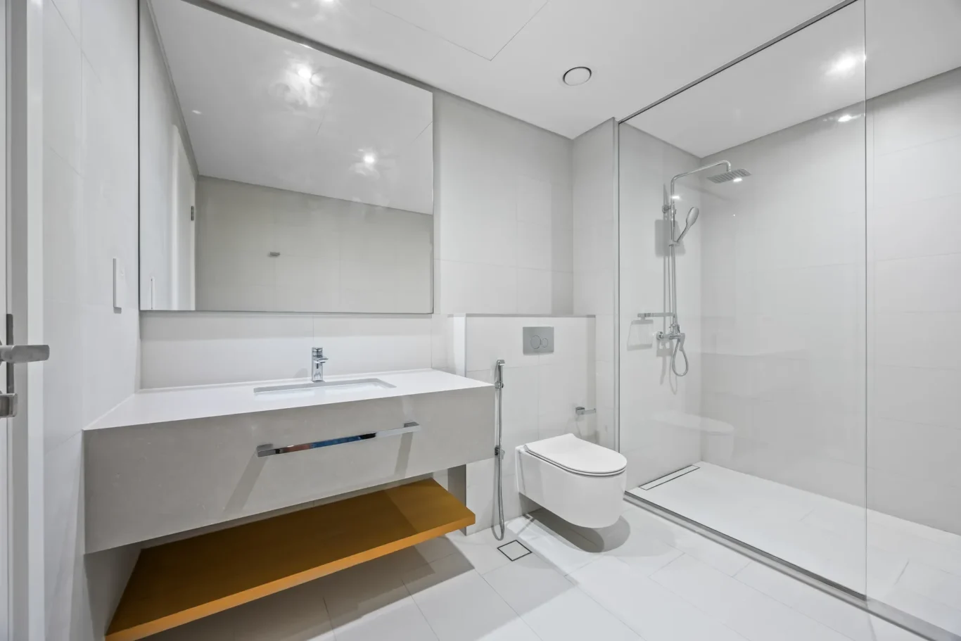 Modern white bathroom with a glass-enclosed shower, wall-hung toilet, and floating vanity with wooden shelf beneath.