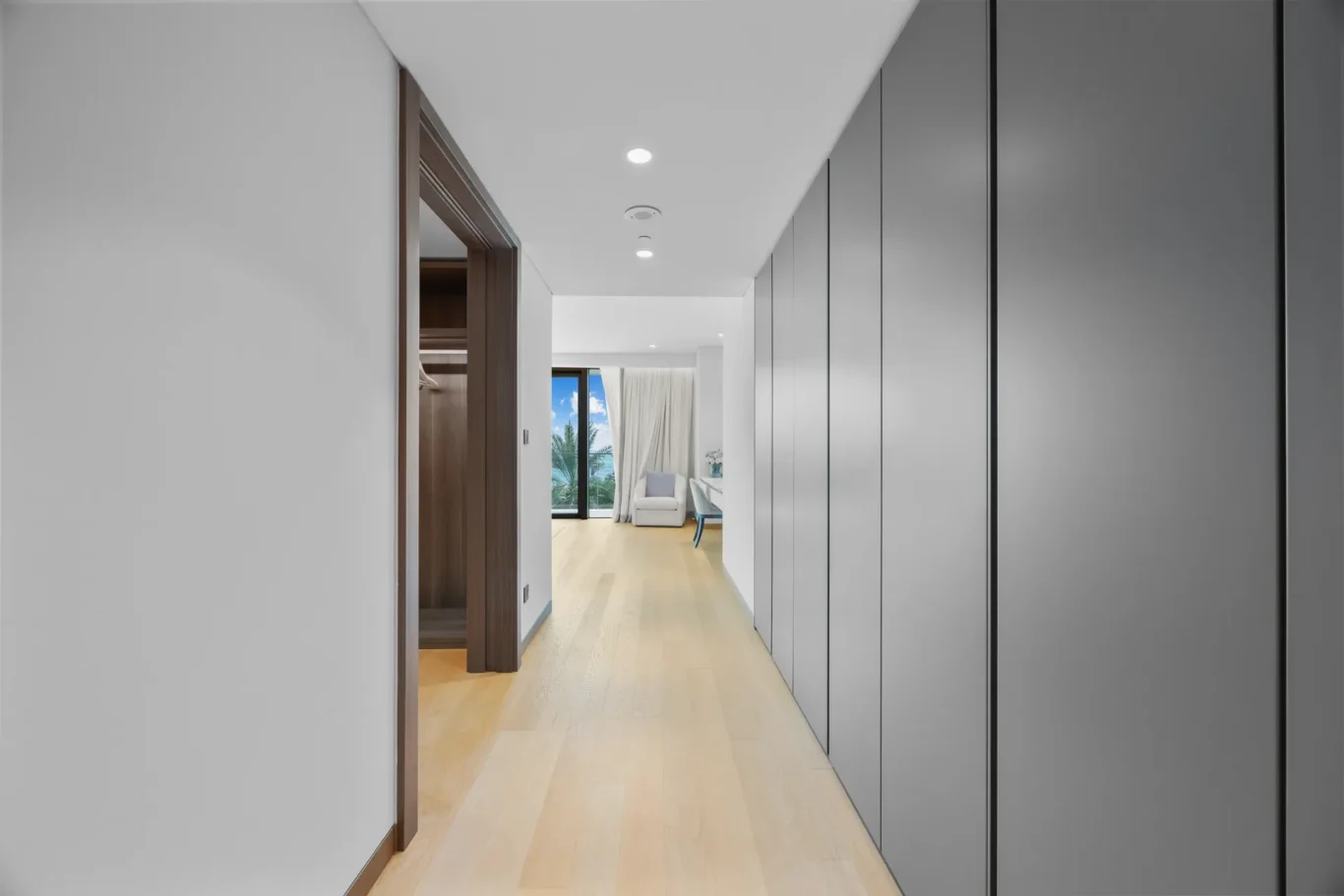 Bright hallway with gray built-in cabinets on the right and a view of a living area at the end.