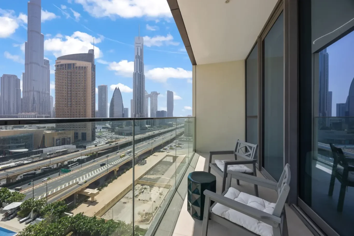 Balcony with two cushioned chairs and a small table overlooking a city skyline and highway below.