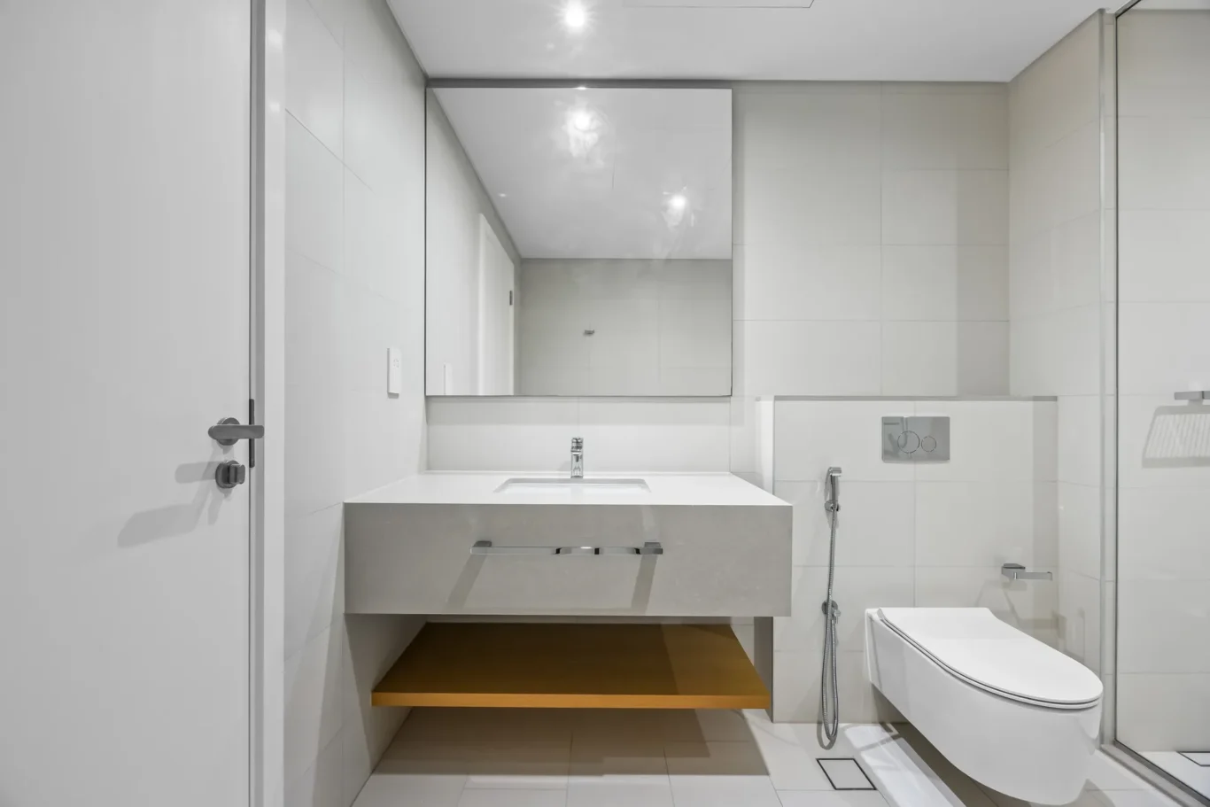Modern white bathroom with a wall-mounted sink, chrome faucet, and large mirror above a floating vanity.