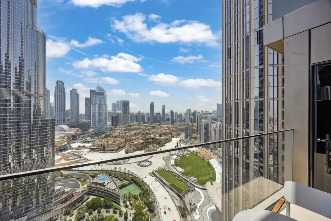 Downtown skyline view from a high-rise balcony, with modern glass towers, a green park, and winding paths below.
