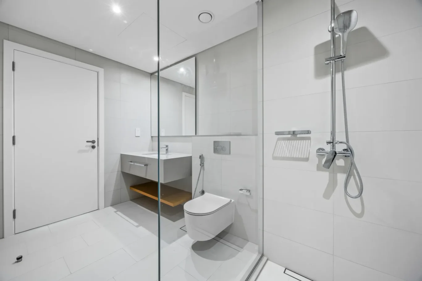 Modern white bathroom with glass shower partition, wall-mounted toilet, and floating sink.