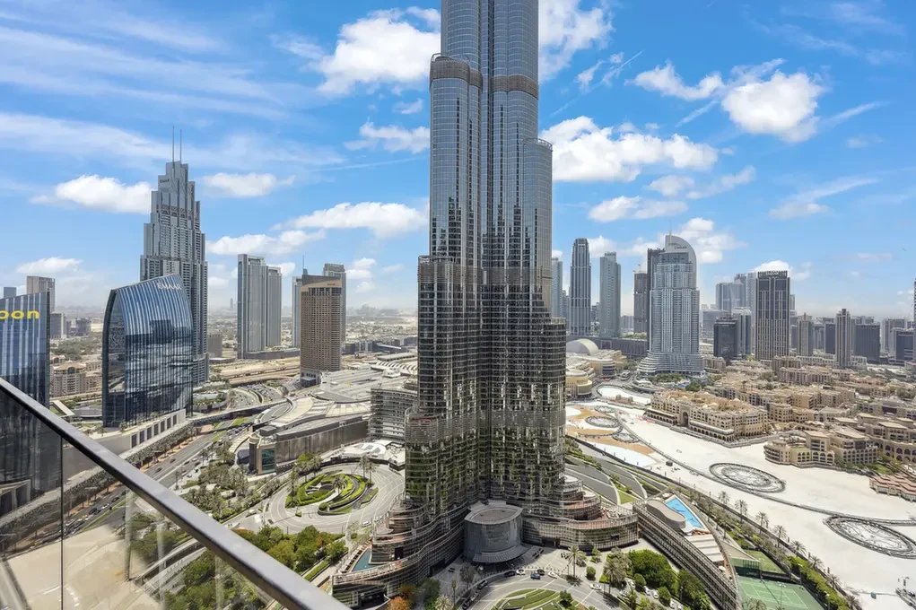 Wide view of Dubai's skyline with the Burj Khalifa center stage and modern glass towers under a blue, partly cloudy sky.