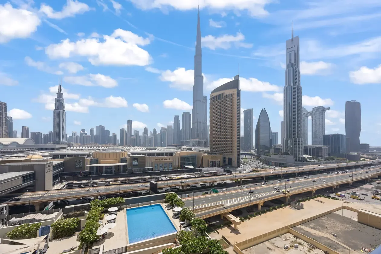 Dubai skyline with skyscrapers, including the tallest tower, seen over an elevated highway and a pool area in the foreground.
