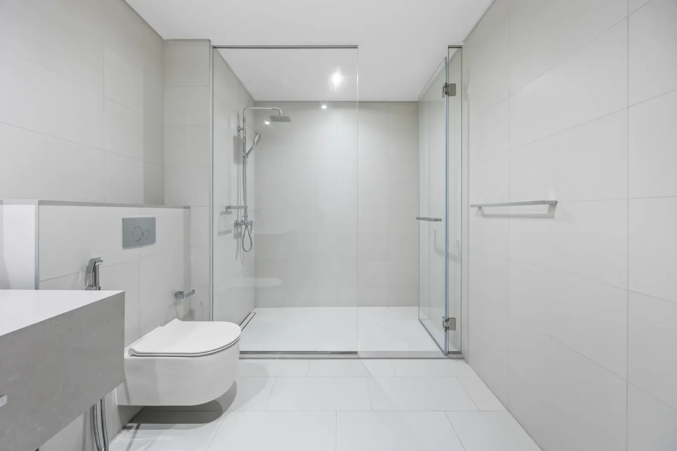 Modern white bathroom with a glass-enclosed shower, wall-mounted toilet, and minimalist sink on the left side.