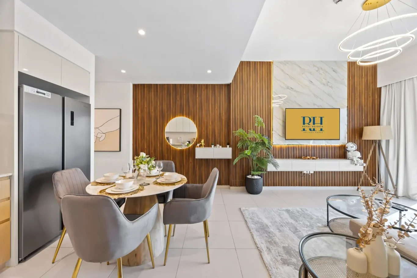 Open-plan dining and living room with a wooden slat wall, round mirror, and a marble feature wall; a TV on the wall displays 'PH ROYAL HEIGHTS' with a slim white cabinet below.
