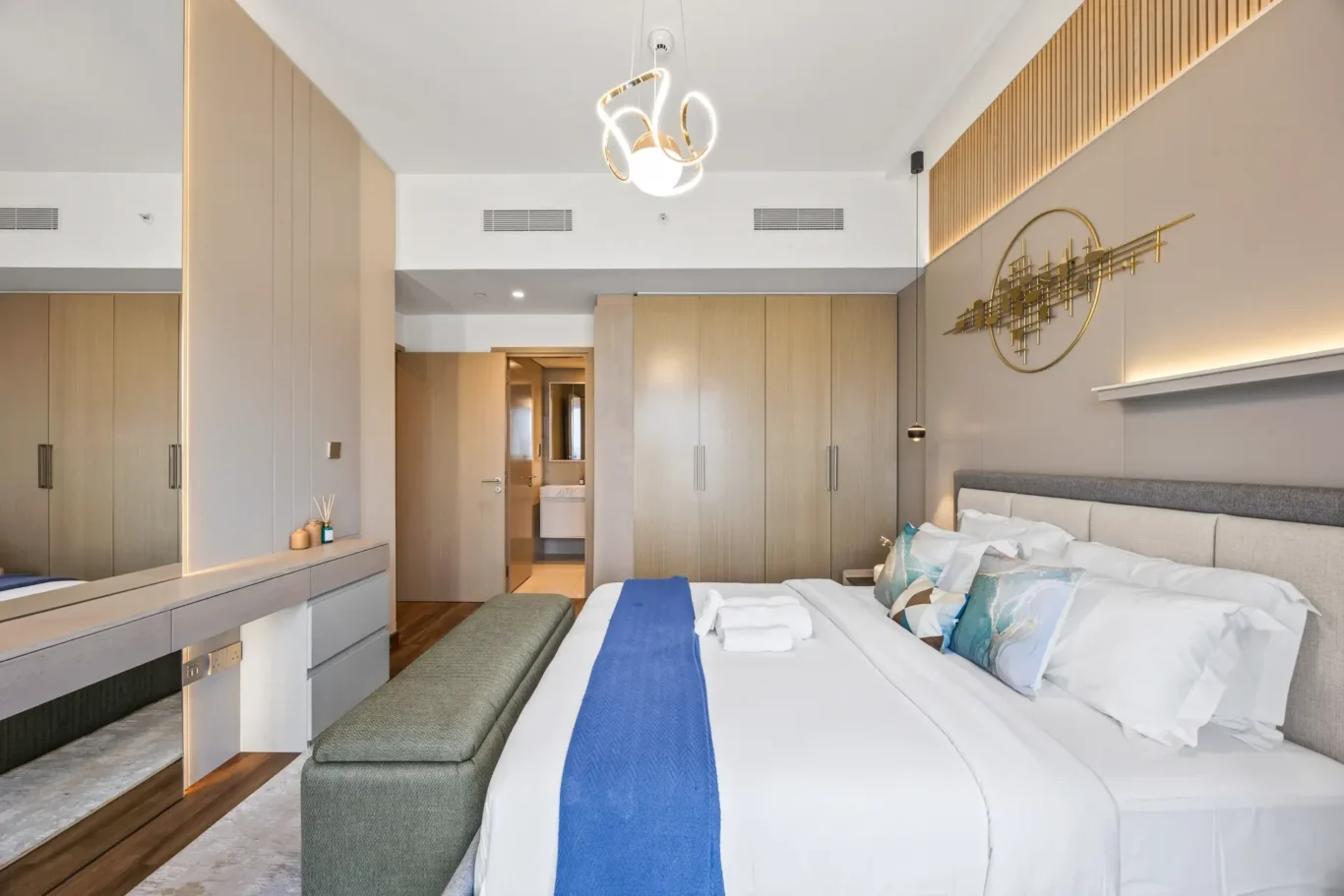 Modern hotel bedroom with two neatly made beds, blue runners, and a long wooden wardrobe wall across the room.