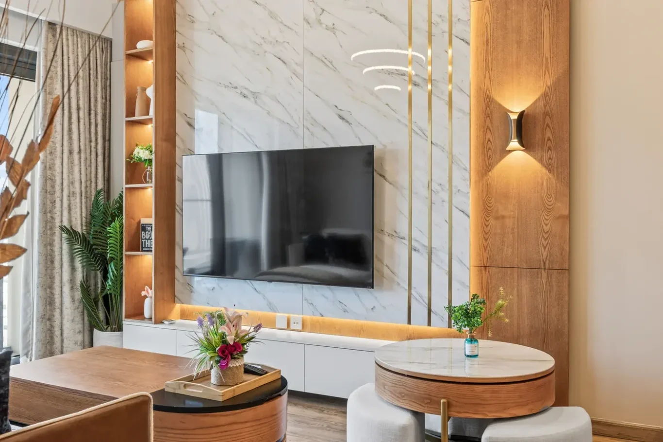 Living room with a wall-mounted TV on a marble backdrop, wood paneling and built-in shelves with plants and decor.