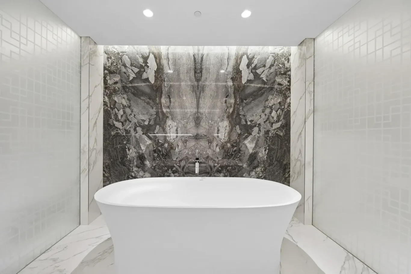 Freestanding white oval bathtub set against a dramatic dark marble wall in a modern spa-like bathroom. Quiet ceiling spotlights overhead.