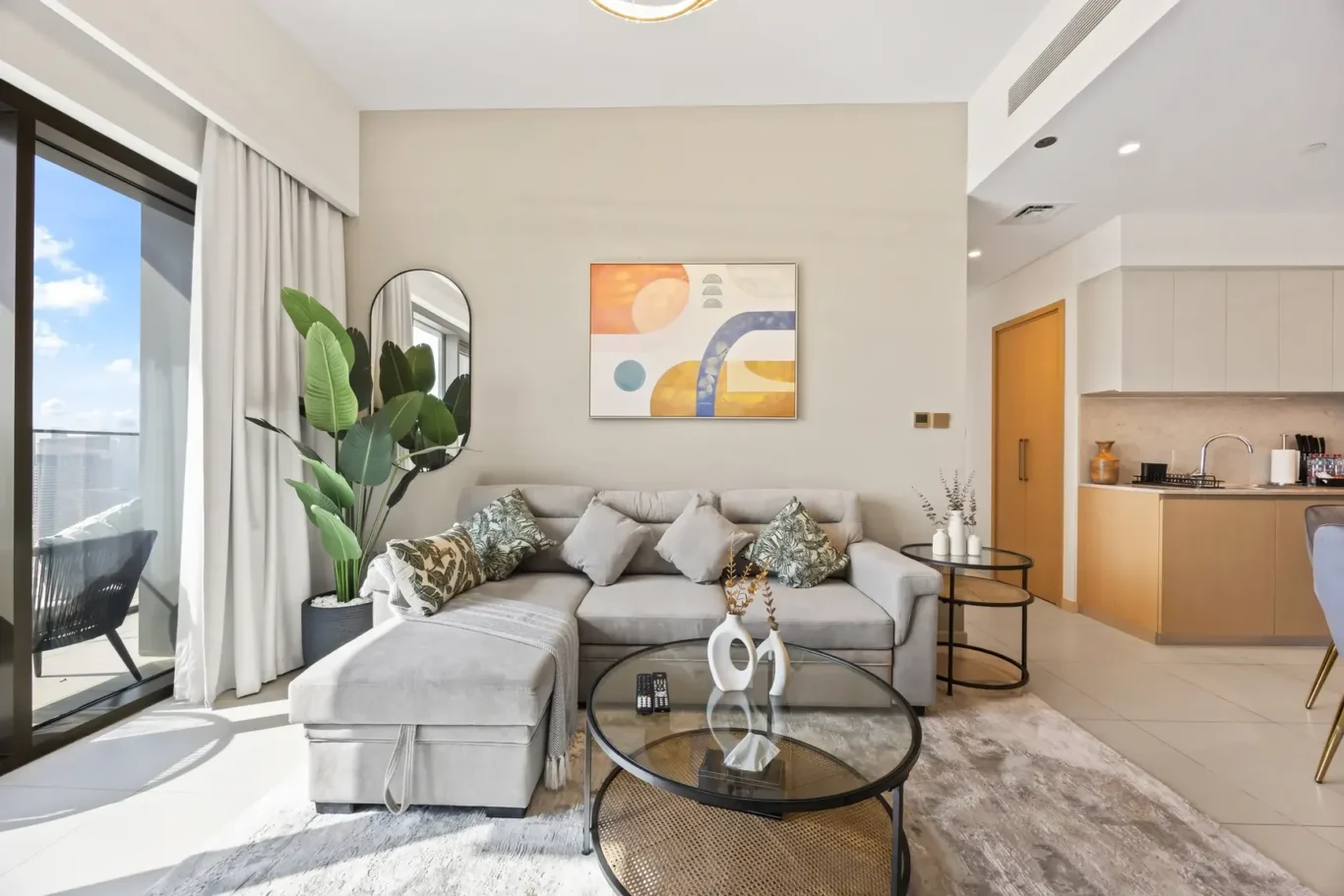 Bright living room with a gray sectional, throw pillows, and a glass coffee table near a balcony door. (informative)
