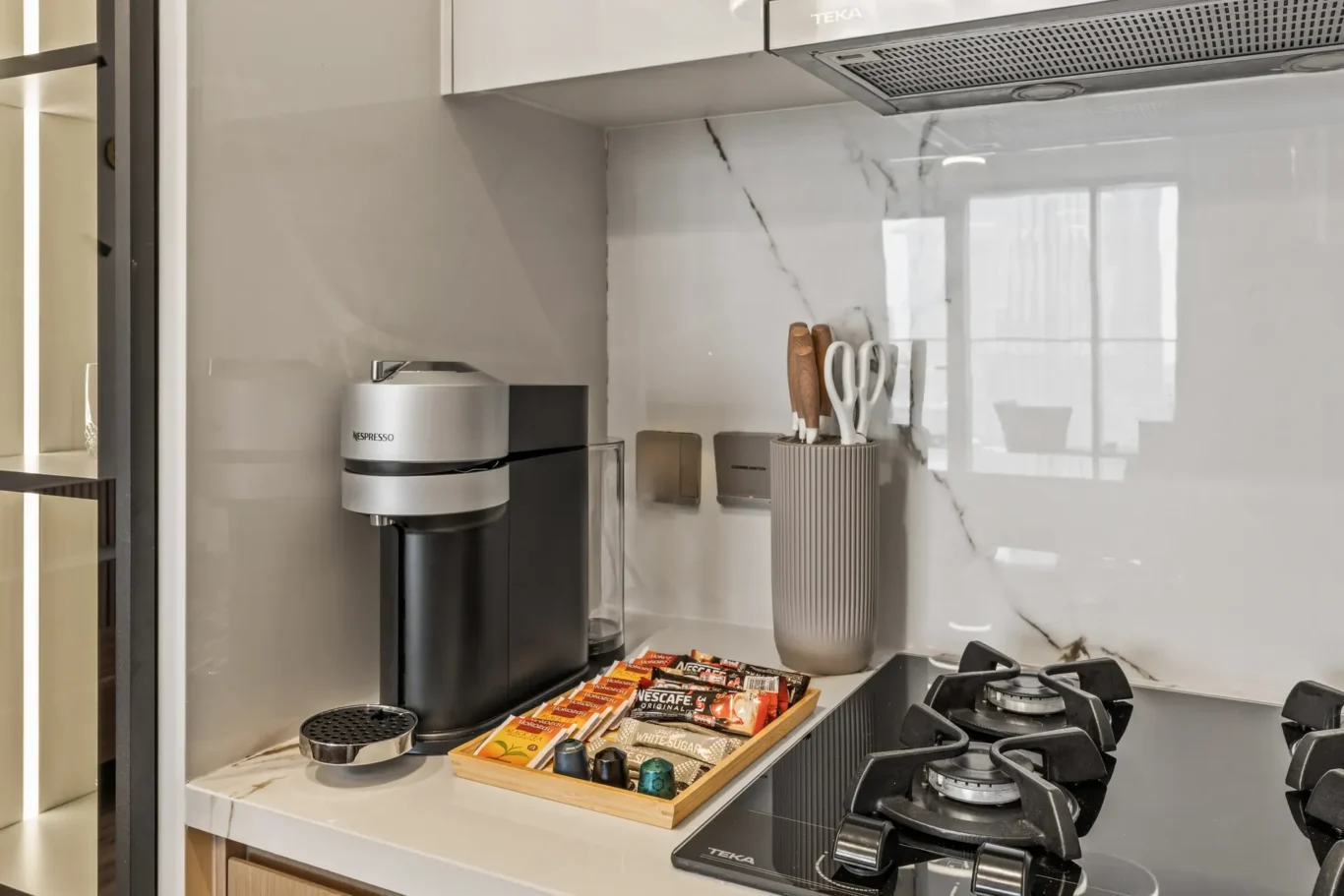Modern kitchen counter with a Nespresso coffee machine, a utensil holder, and a tray of coffee sachets near a gas stove.