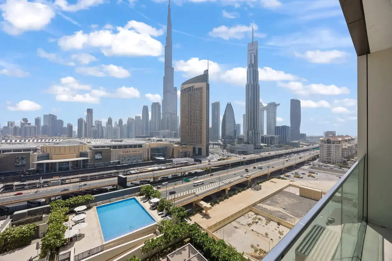 View of Dubai's skyline with skyscrapers and a highway, seen from a balcony overlooking a pool and sun loungers in the foreground.