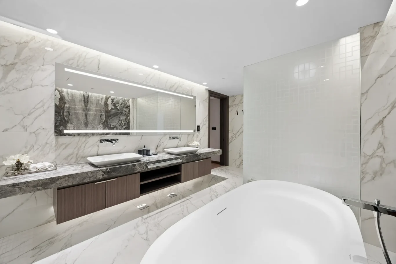 Luxurious marble bathroom with double vessel sinks, backlit mirror, and a freestanding tub edge