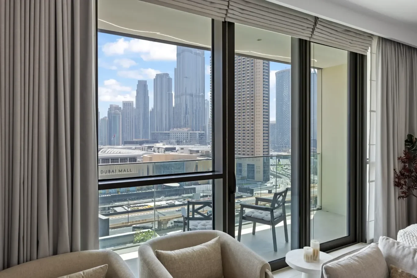 Living room with large glass doors opening to a balcony, overlooking Dubai skyscrapers and the Dubai Mall beyond.