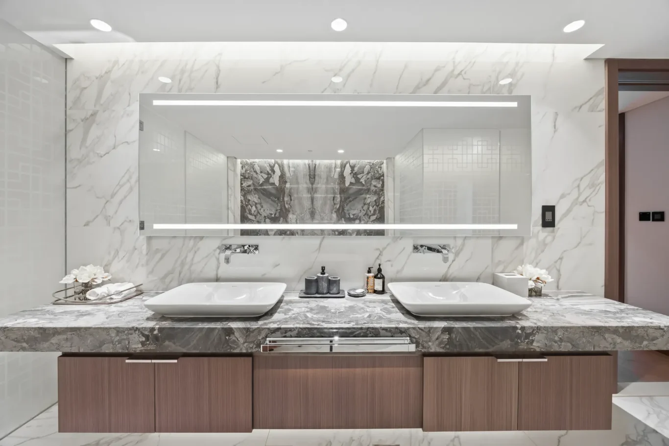 Luxurious bathroom vanity with two rectangular vessel sinks on a marble countertop and a large backlit mirror.