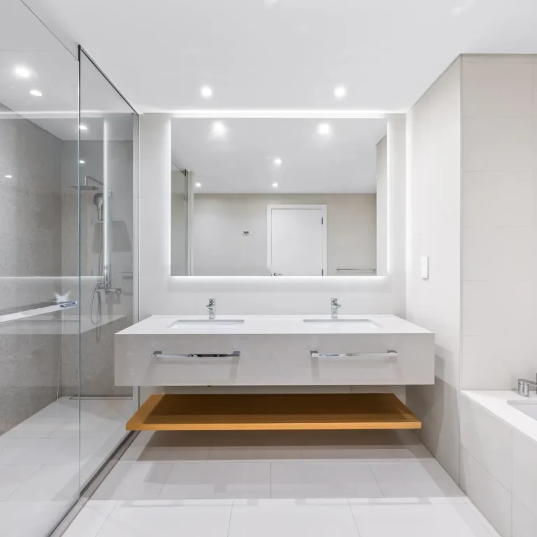 Modern bathroom with double sinks and backlit rectangular mirror, glass-enclosed shower on the left and a bathtub on the right.