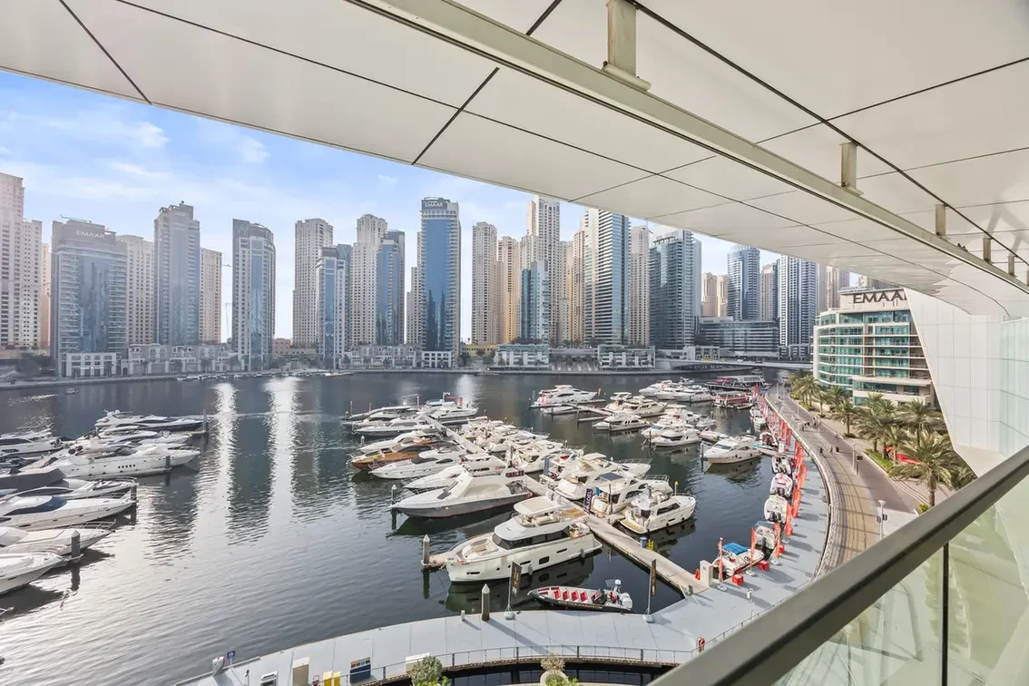 Marina with numerous white yachts docked at piers and high-rise glass buildings in the background.