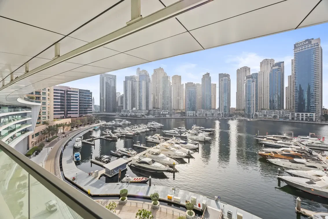 Harbor with numerous luxury yachts docked along a marina, with modern high-rise buildings in the background.