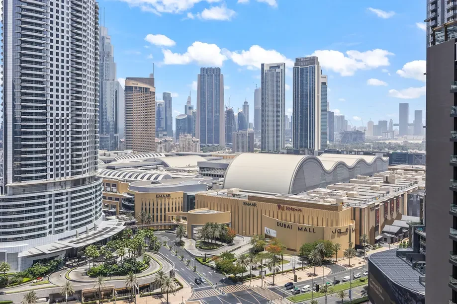 Wide view of Dubai's skyline with tall skyscrapers and the Dubai Mall complex in the foreground under a blue sky