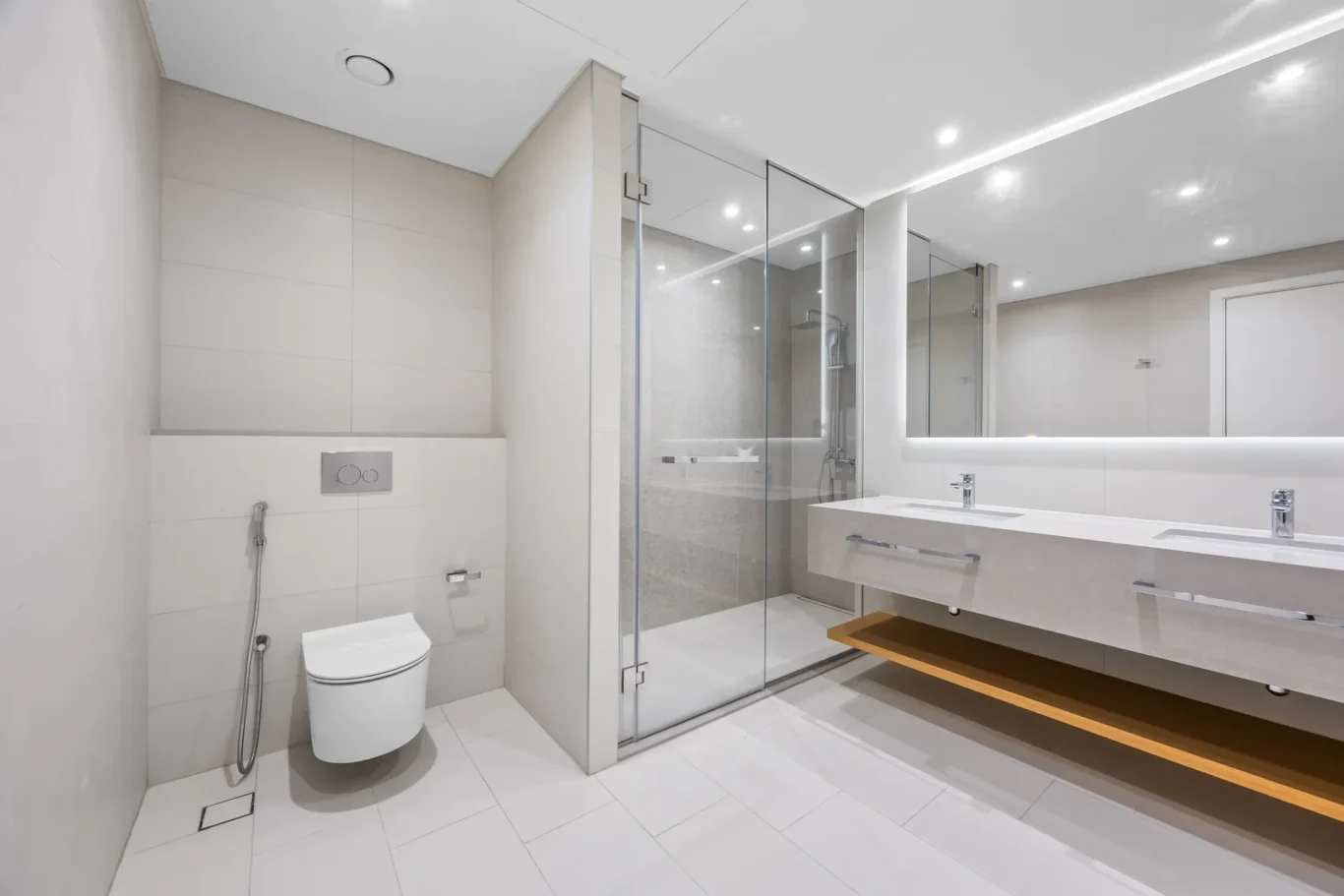 Modern white bathroom with a glass-enclosed shower, dual sinks, and a wall-mounted toilet in a minimalist design.