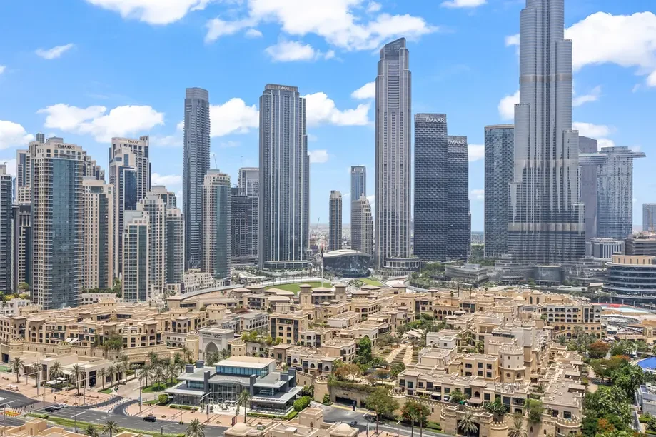 Skyline with numerous tall glass skyscrapers behind a uniform area of beige low-rise buildings under a blue sky.