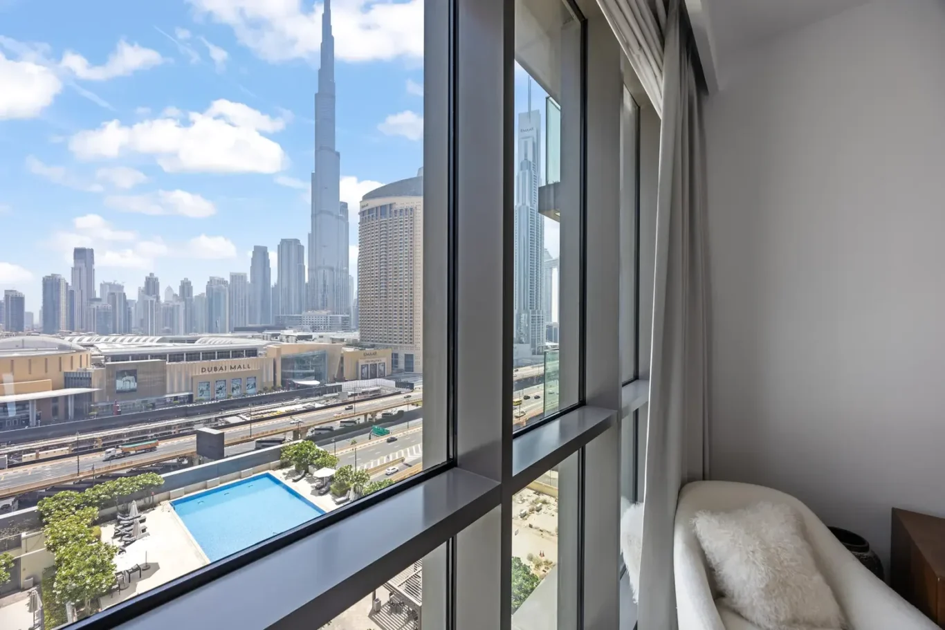 Hotel room with floor-to-ceiling windows overlooking Dubai's skyline, including the Burj Khalifa and Dubai Mall below.