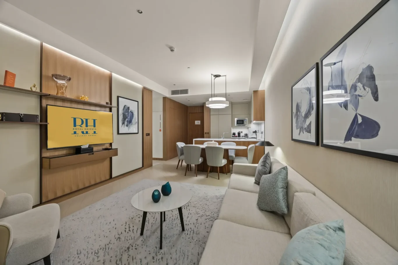 Open-plan living and dining area: beige sofa, round marble coffee table with teal vases, and a dining table near the kitchen.