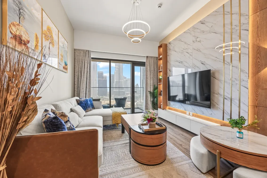 Bright modern living room with a white sectional, marble accent wall, wall-mounted TV, and city skyline visible through large windows.