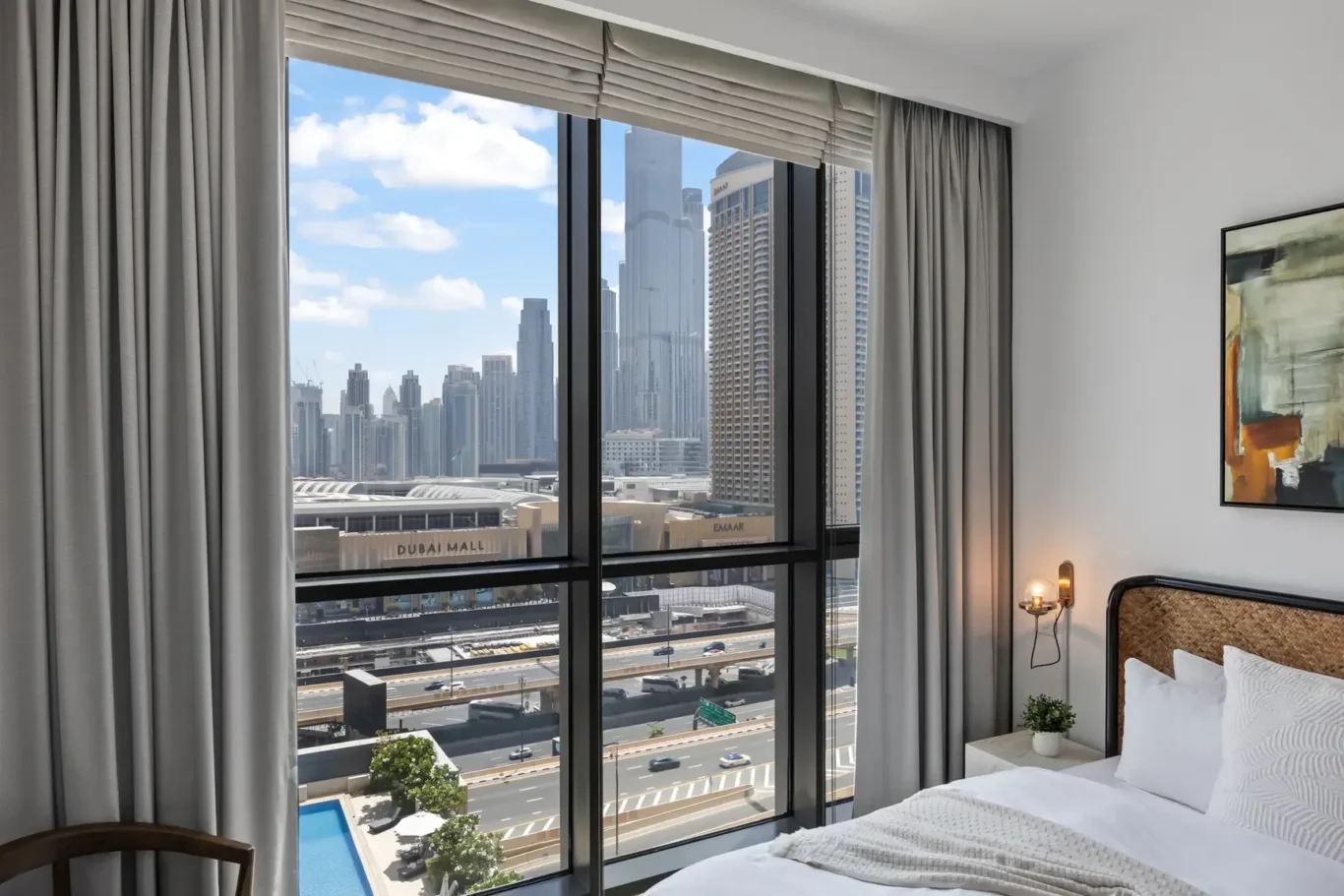 Hotel room with a large window overlooking Dubai's skyline and road below; bed on the right side of the frame.