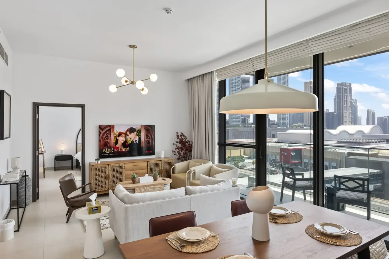 Bright open-concept living and dining area with a large city-view window, beige seating, and a wooden dining table set for four.