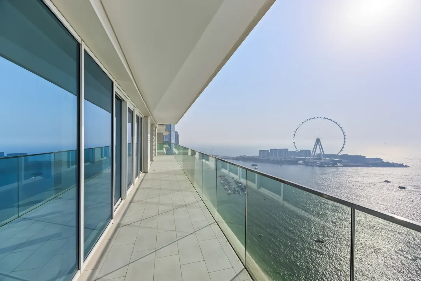 Balcony with glass railing overlooking water and a distant Ferris wheel on a sunny day