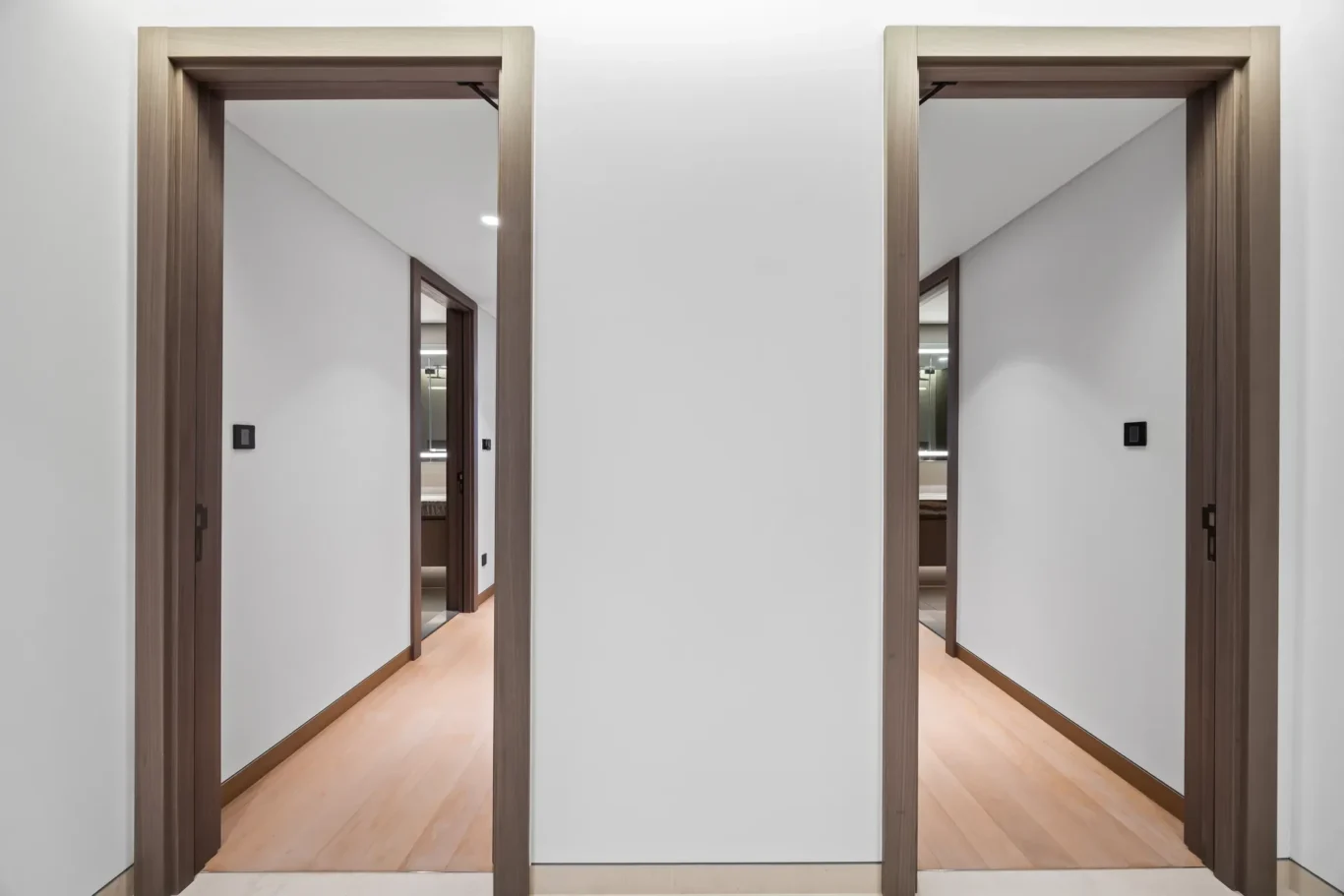 Modern hallway with twin wooden-framed doorways, light wood flooring, white walls