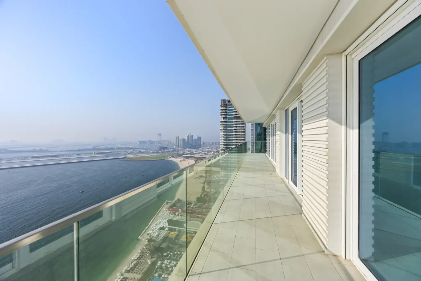 Balcony of a modern high-rise overlooking the blue sea and distant city skyline.