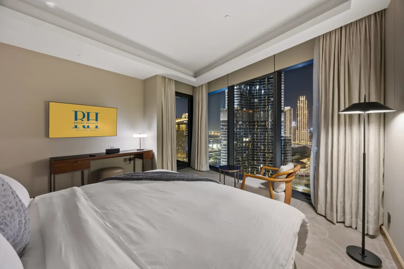 Hotel room at night with two white beds and a city skyline visible through floor-to-ceiling windows