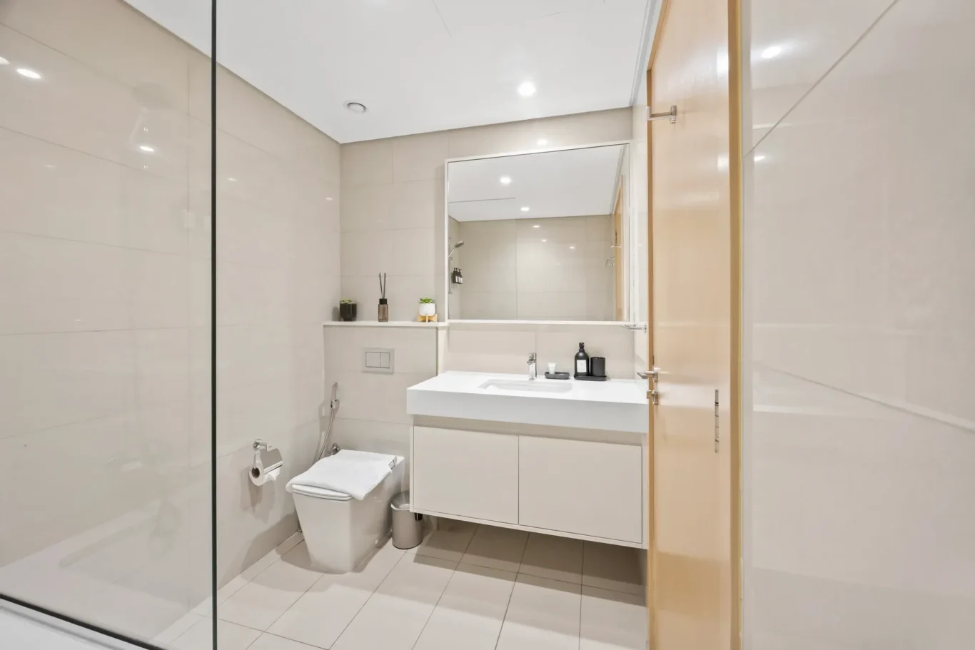 Modern white bathroom with a wall-mounted vanity, large mirror, toilet and glass shower enclosure.