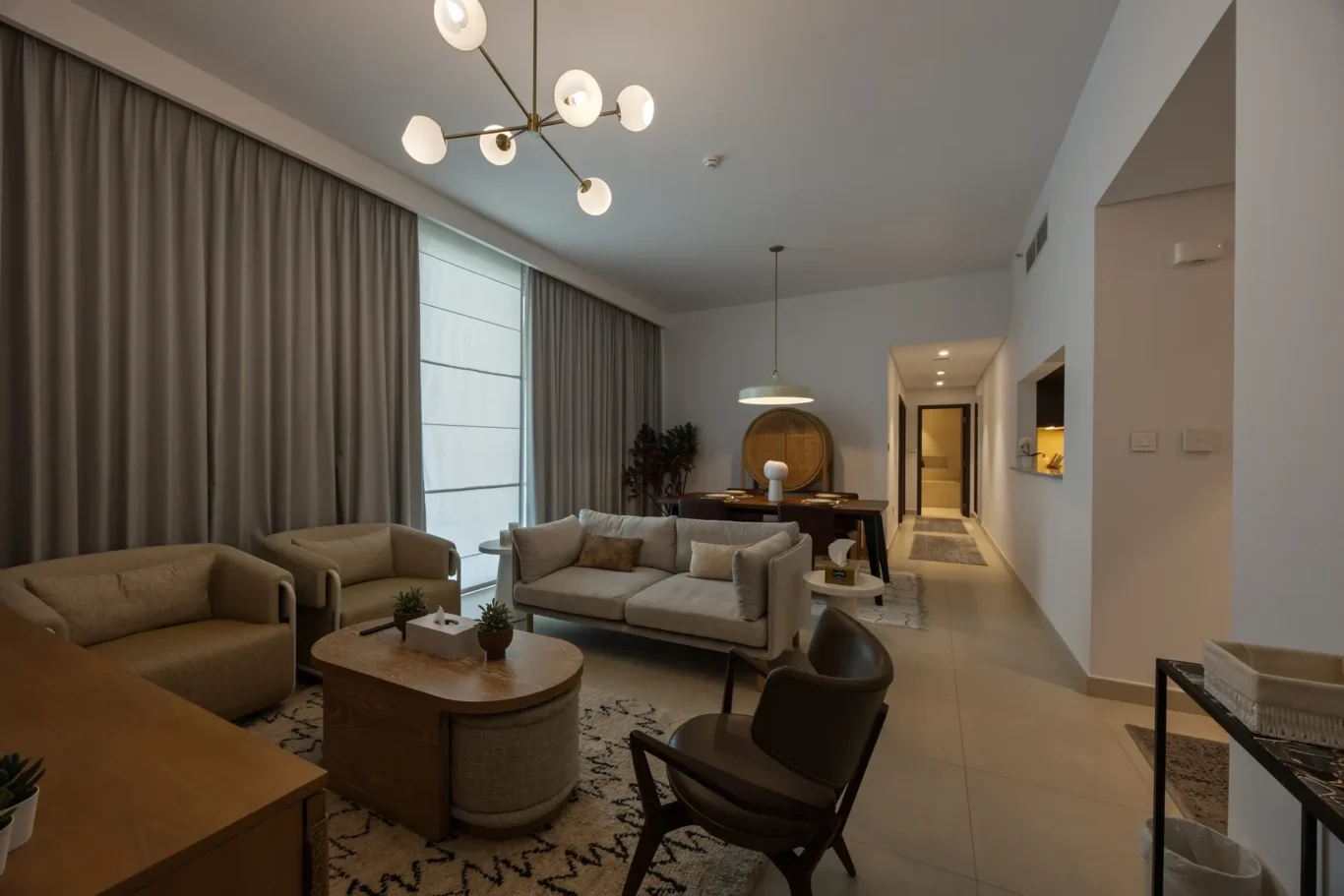 Open-concept living room with beige sofas, two round coffee tables, and large gray curtains along a wall of windows.