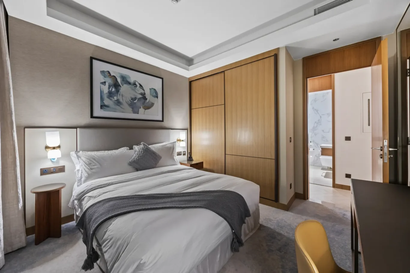 Hotel bedroom with a large bed, grey bedding, and a framed abstract painting above the headboard.