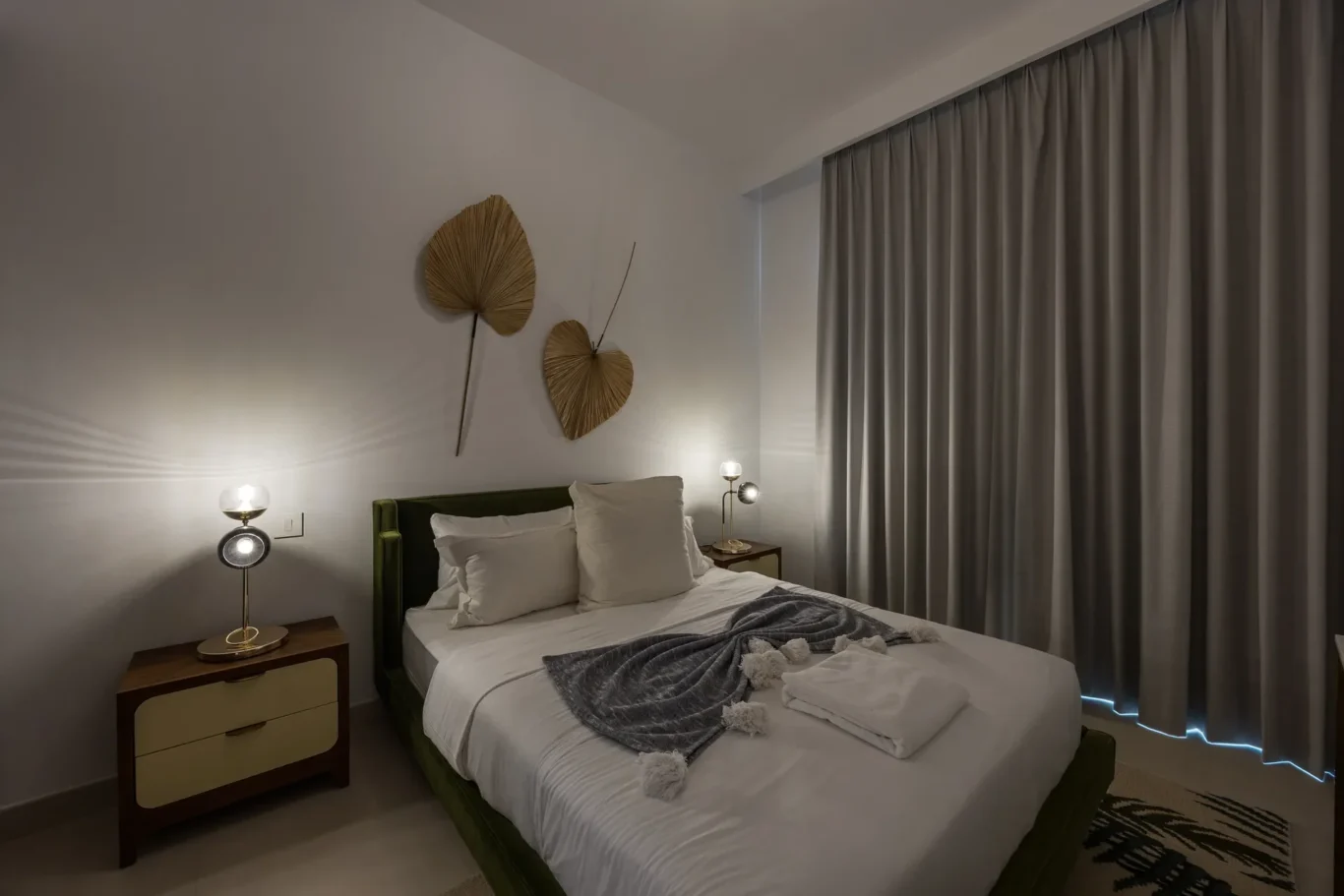 Cozy hotel bedroom with a bed, two bedside lamps, and palm-leaf wall art above the headboard.