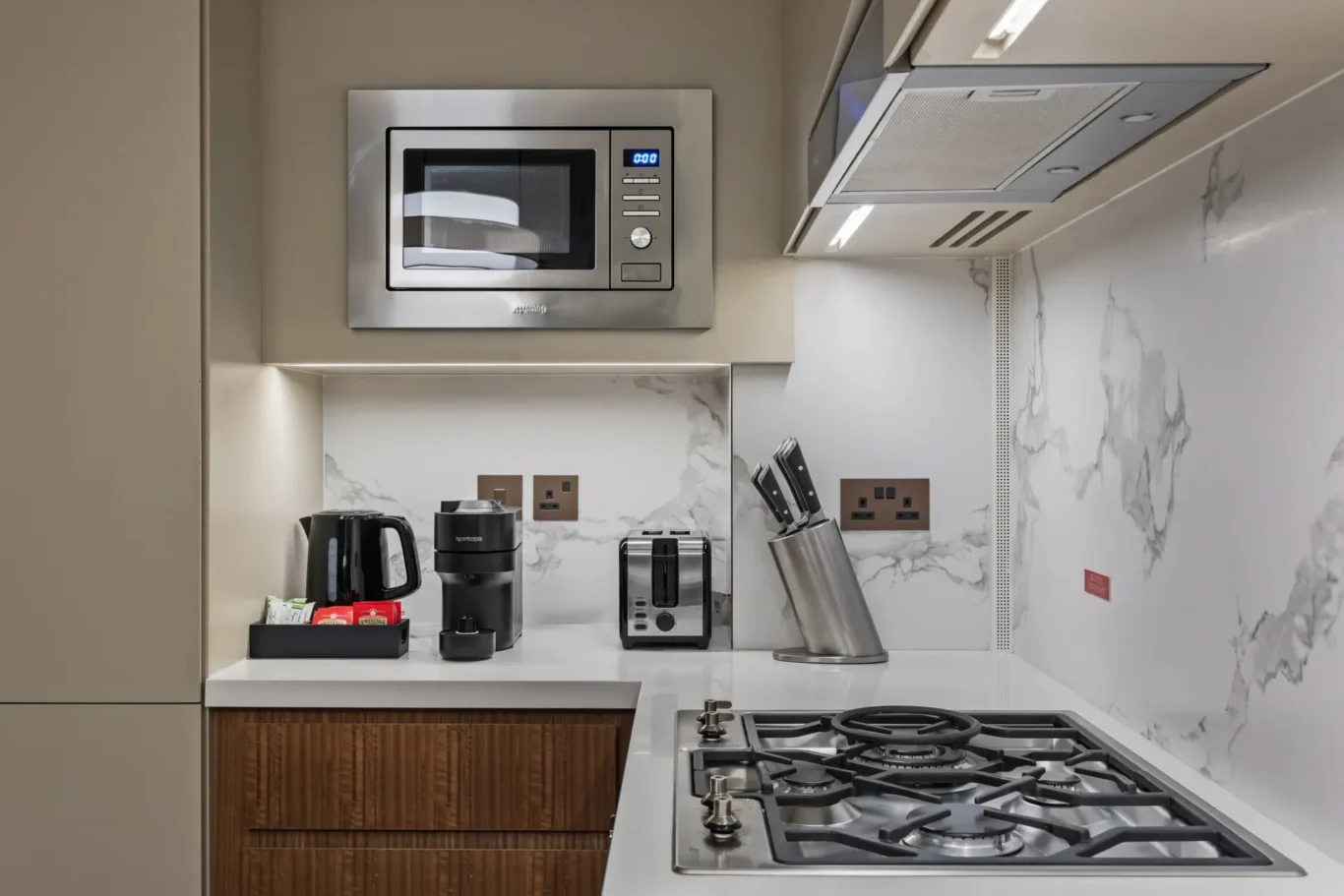 Modern kitchen counter with stainless steel microwave, kettle, and toaster, marble backsplash, and knife block above a gas stove