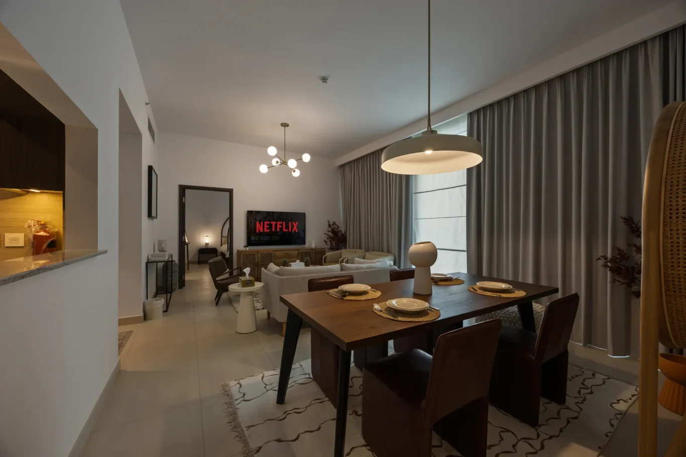 Open-concept living and dining area with a wooden six-seat table, beige sofa, and a Netflix TV on the wall.