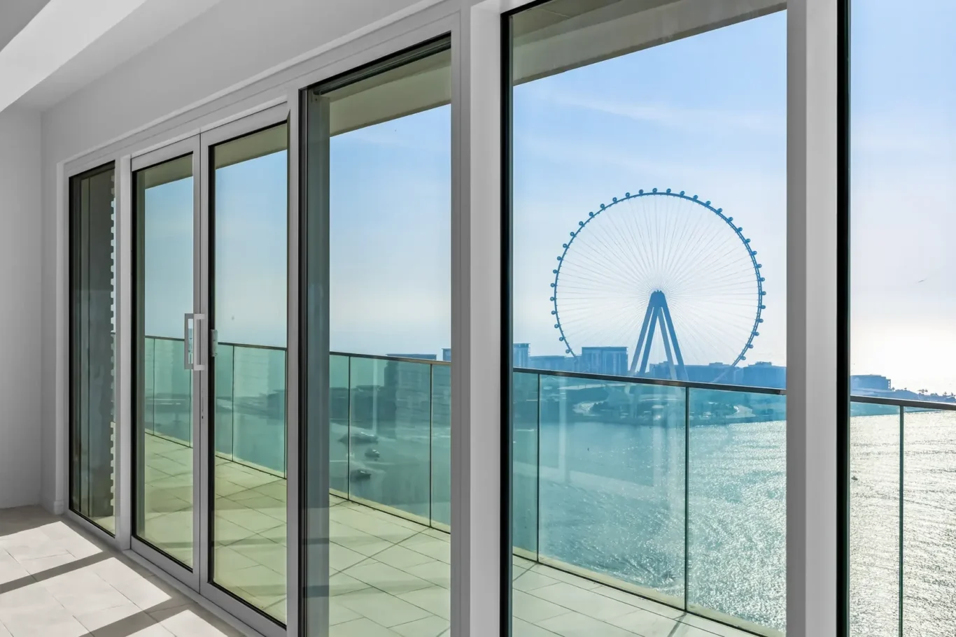Indoor balcony with floor-to-ceiling glass doors; view of a blue Ferris wheel over the water.